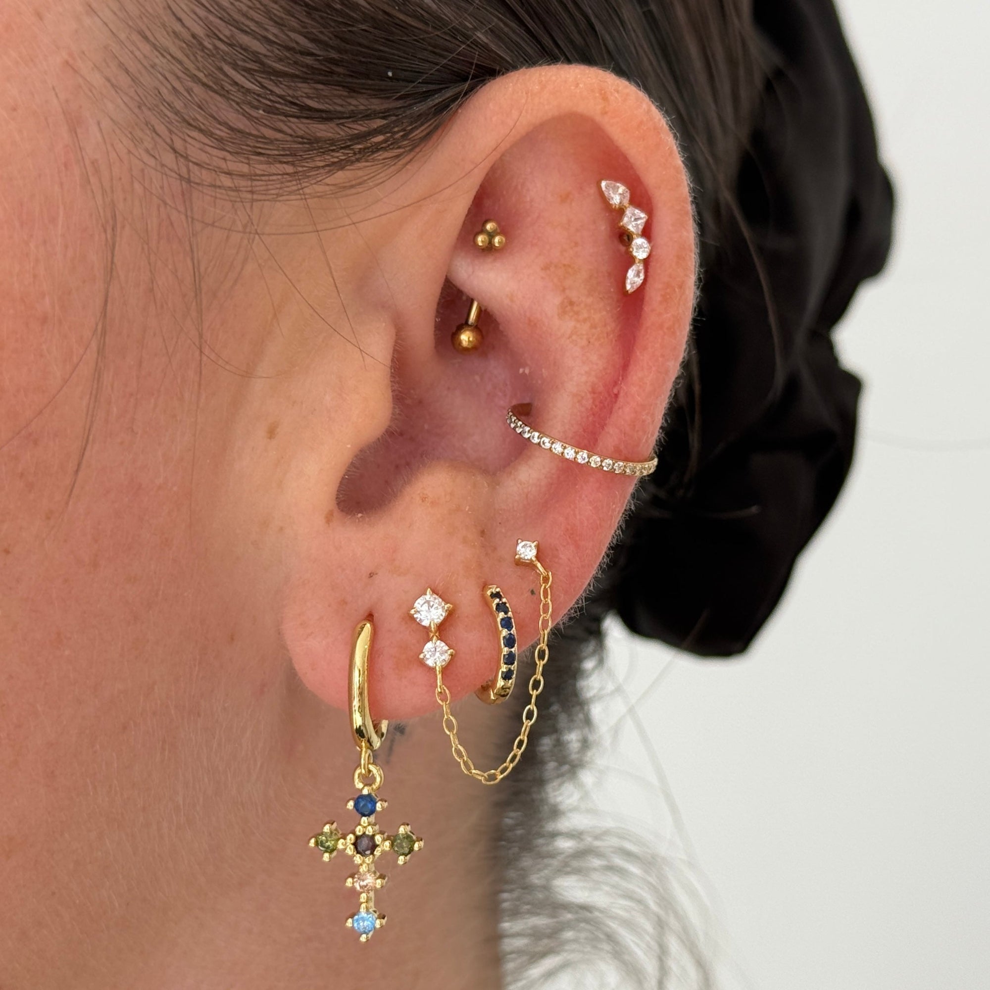 Close-up of an ear with multiple gold and diamond earrings on a neutral background