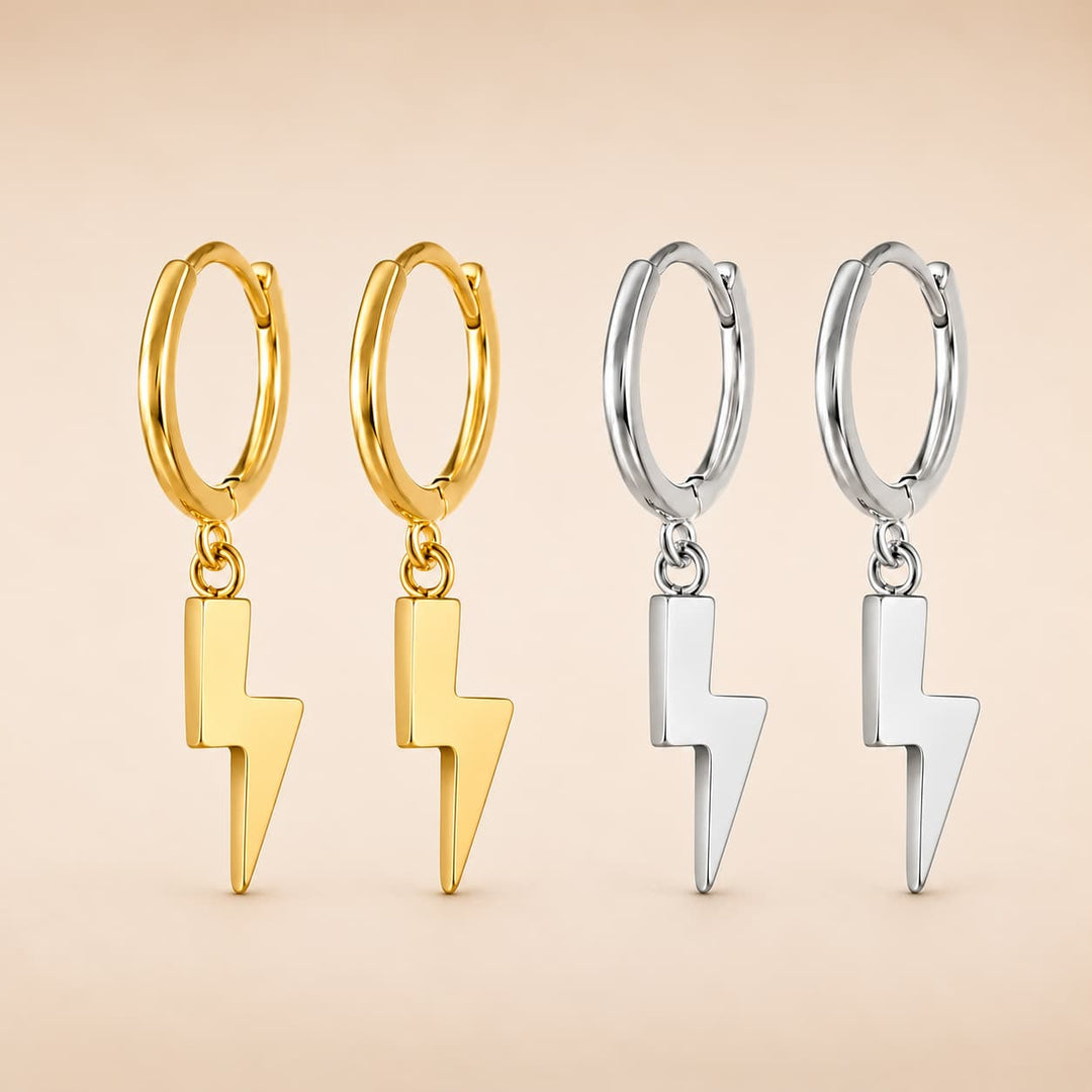 Four small hoop earrings with dangling lightning bolt charms, shown in two metal finishes: gold on the left and silver on the right, against a soft beige background.