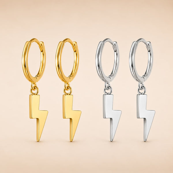Four small hoop earrings with dangling lightning bolt charms, shown in two metal finishes: gold on the left and silver on the right, against a soft beige background.