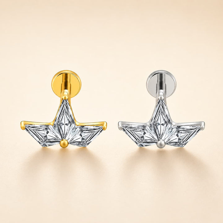 Two geometric star-shaped stud earrings with clear faceted stones, shown side by side in yellow gold and silver-tone metal finishes on a warm beige background.