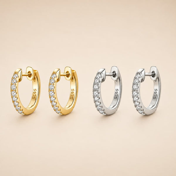 Four 925 sterling silver huggie hoop earrings, two in yellow gold and two in silver, each adorned with a row of clear pavé-set cubic zirconia stones, arranged on a warm beige background.