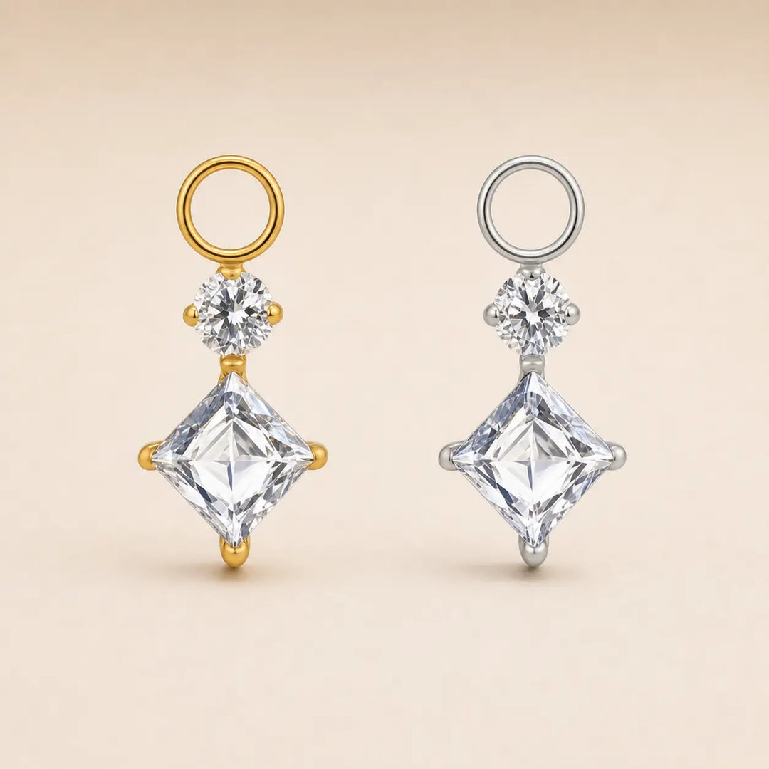 Two diamond drop earrings displayed side by side on a light beige background. One earring features a gold-plated setting with a round gold ring, a small round diamond, and a larger square-cut diamond.