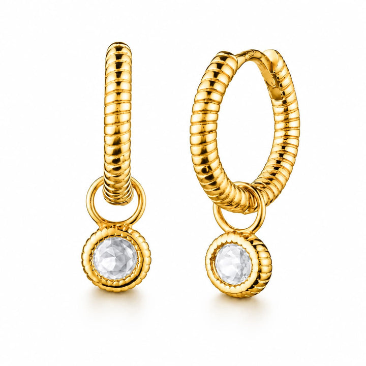 A pair of gold huggie hoop earrings with a textured rope-like vertical bar, a small connecting ring, and a round bezel-set clear gemstone dangle, shown on a white background.