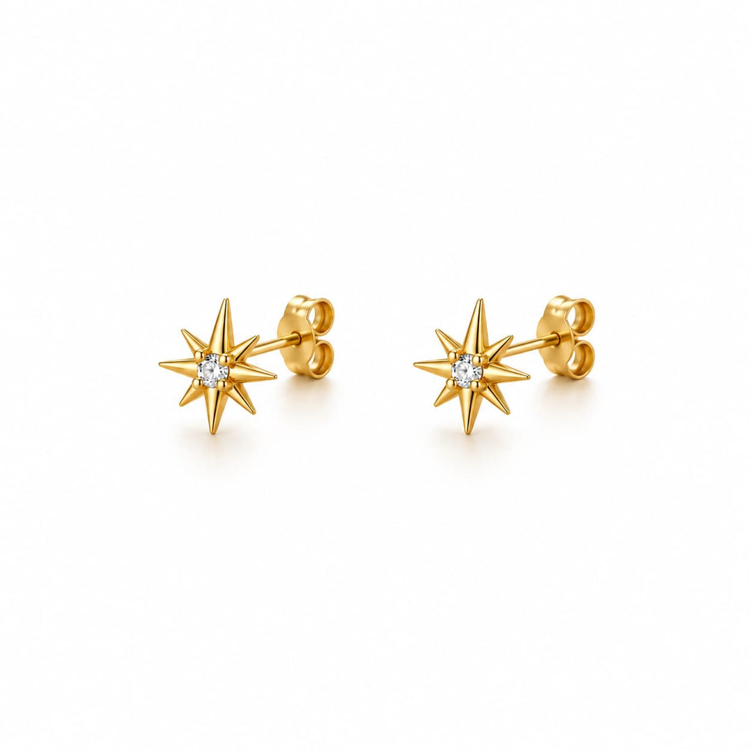 A pair of gold starburst stud earrings, each featuring a small clear round-cut gemstone at the center, displayed on a clean white background.