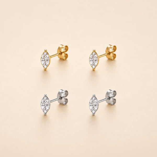 Four marquis-cut stud earrings with clear gemstones, shown in both yellow gold and silver metal finishes on a warm beige background.