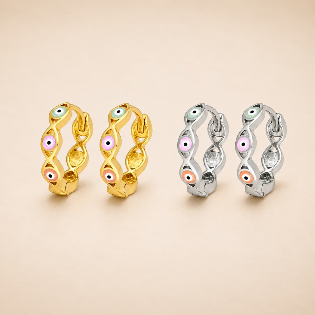 Four huggie hoop earrings with an evil eye motif, shown in two metal finishes: yellow gold on the left and silver on the right. Each earring features a twisted design with small enamel evil eye details in pink, orange, green, and white.