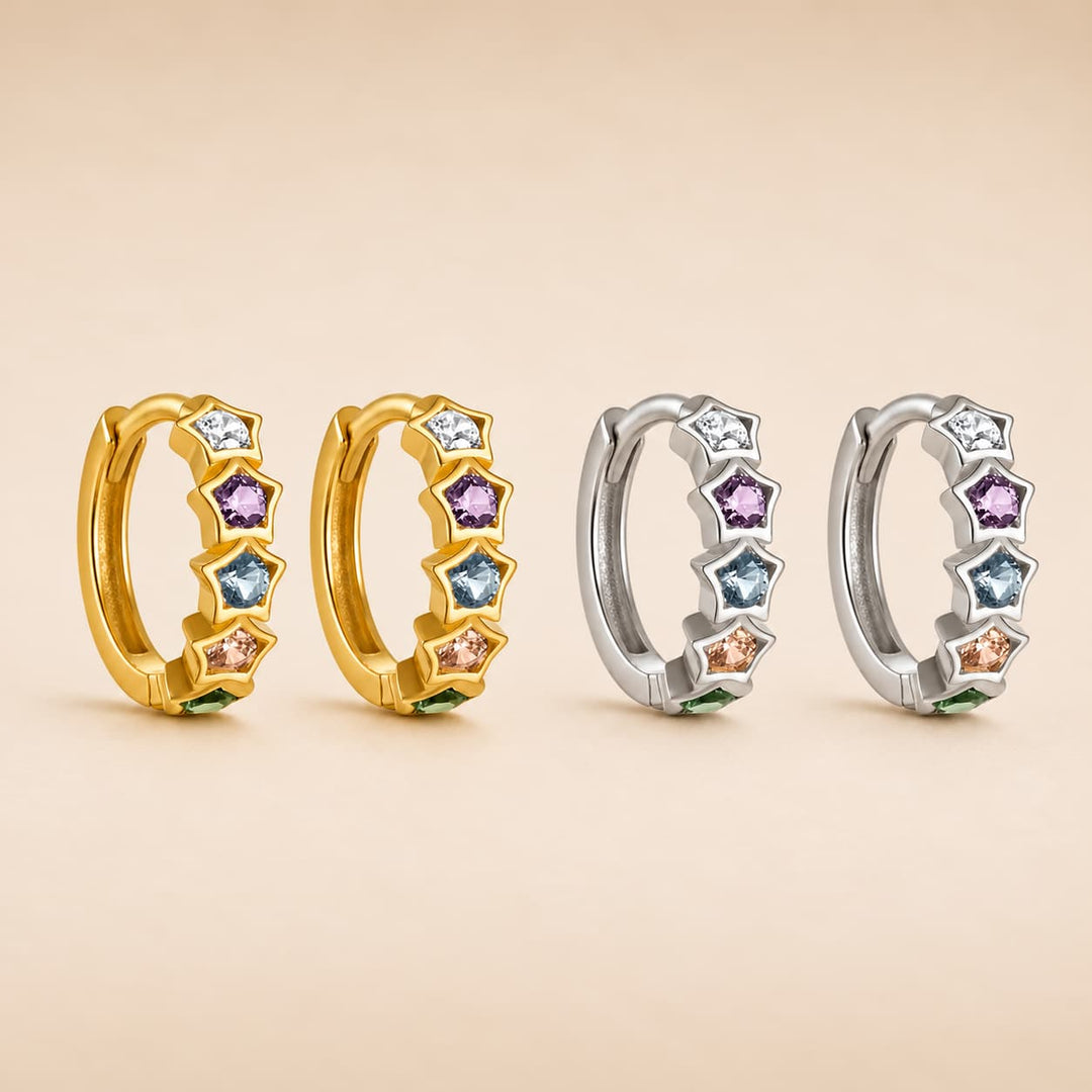 Four huggie hoop earrings arranged in two pairs on a warm beige background. Each earring features a curved gold or silver band set with star-shaped bezel settings holding small round and faceted gemstones in white, light blue, purple, pink, and green colors.