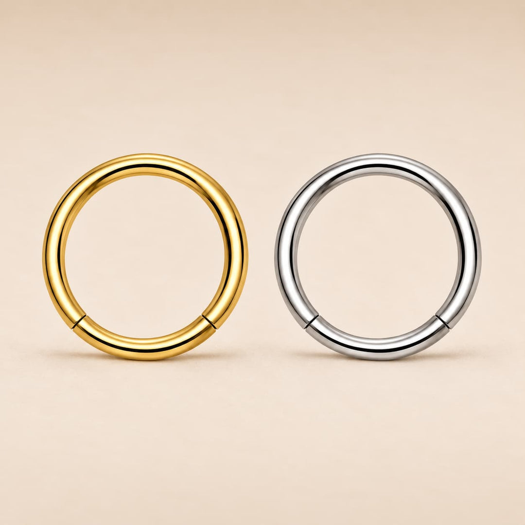 Two metal hoop rings, one in polished yellow gold and one in polished silver, displayed side-by-side on a warm beige background.