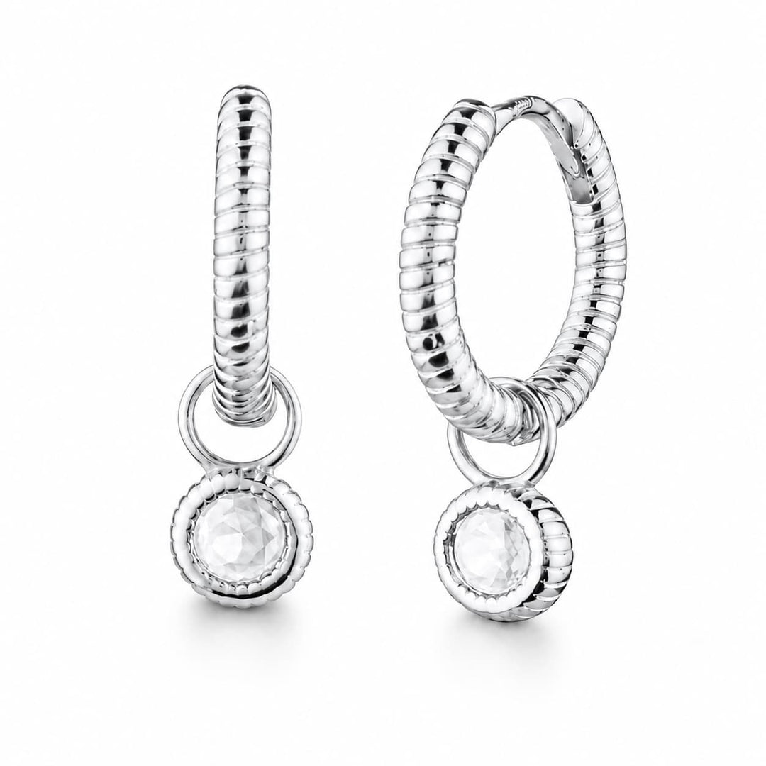A pair of silver huggie hoop earrings with a textured snake-like band, a small connecting ring, and a dangling round bezel-set clear gemstone, shown on a white background.