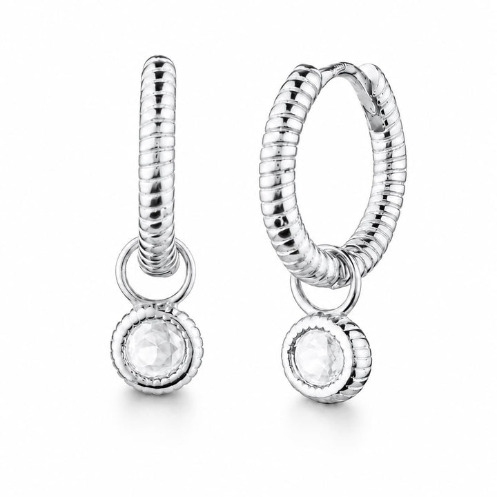 A pair of silver huggie hoop earrings with a textured snake-like band, a small connecting ring, and a dangling round bezel-set clear gemstone, shown on a white background.