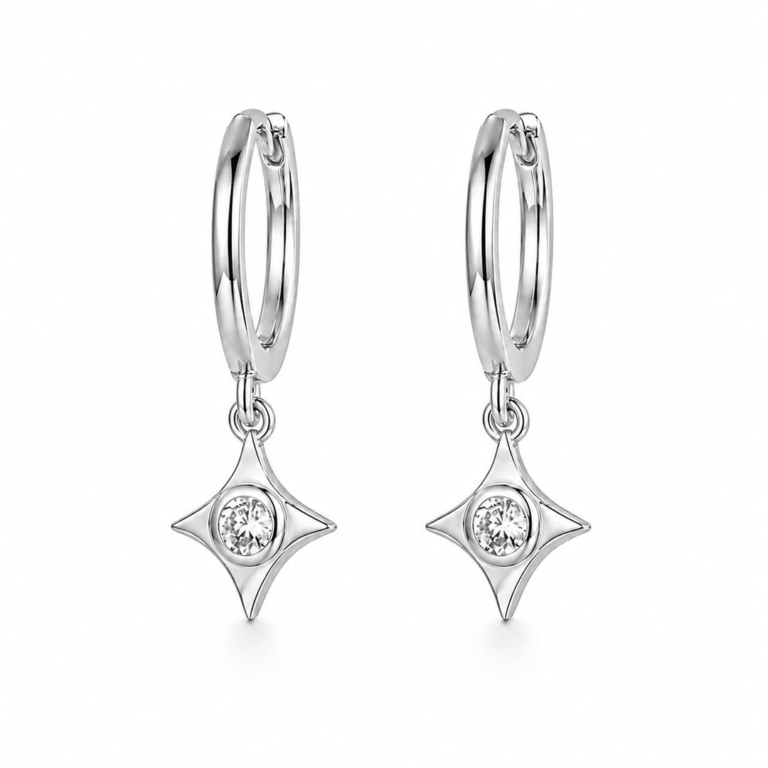 A pair of silver huggie hoop earrings with dangling four-pointed star charms, each featuring a small clear round gemstone in the center, set against a plain white background.