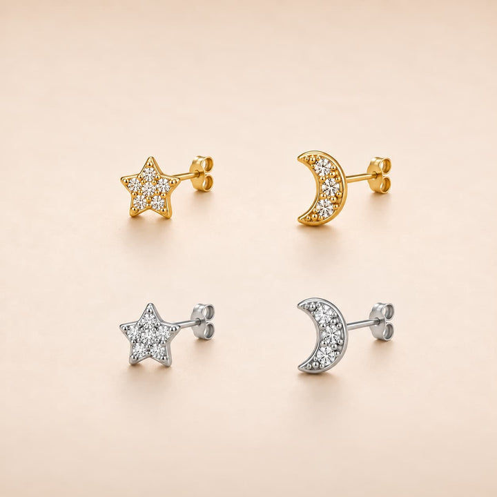Four small stud earrings arranged in a 2x2 grid on a warm beige background: two gold-tone star and moon earrings with clear stones, and two silver-tone star and moon earrings with clear stones.