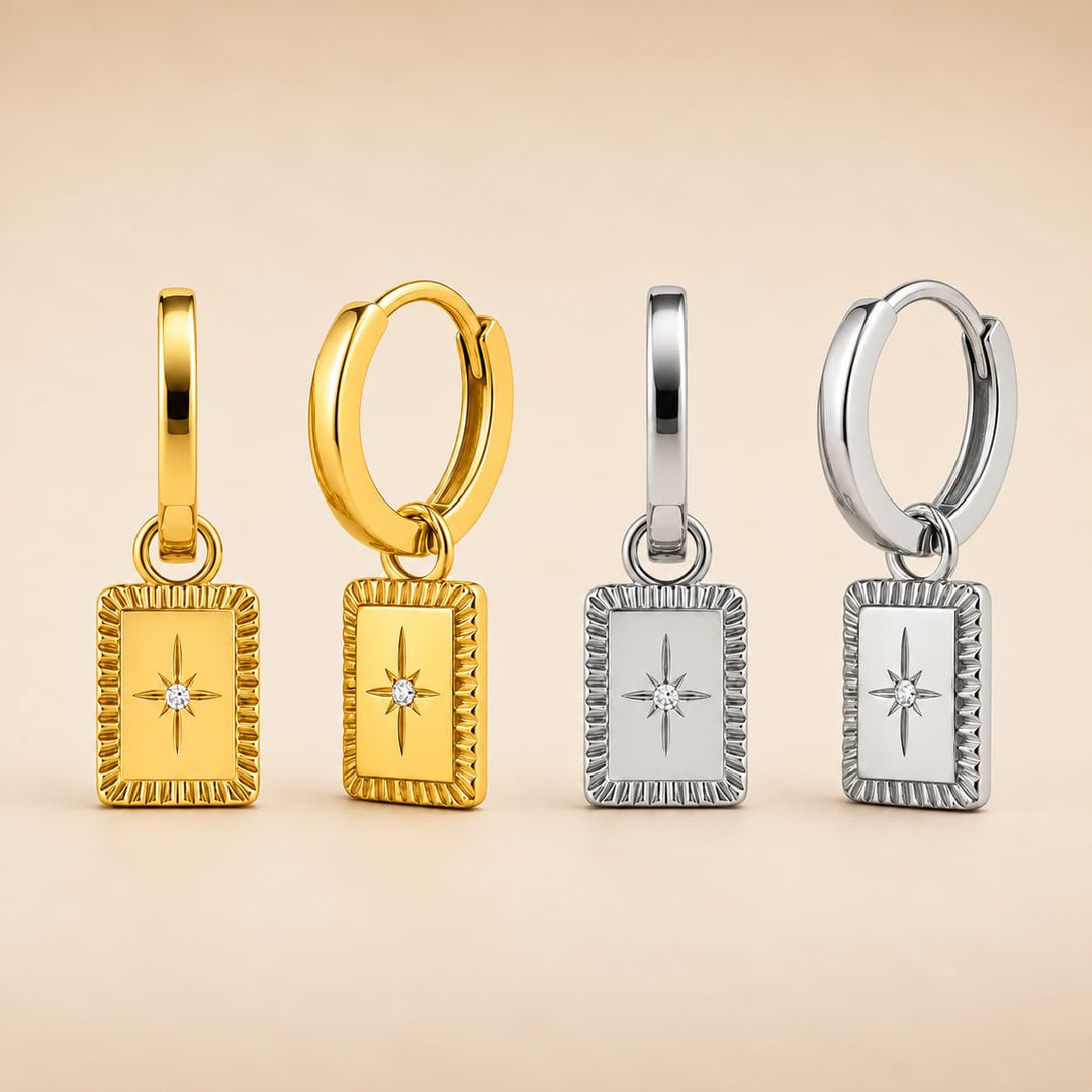 Four rectangular huggie hoop earrings with starburst charms are displayed in two colorways: yellow gold and silver. Each earring features a small clear gemstone in the center of the starburst.