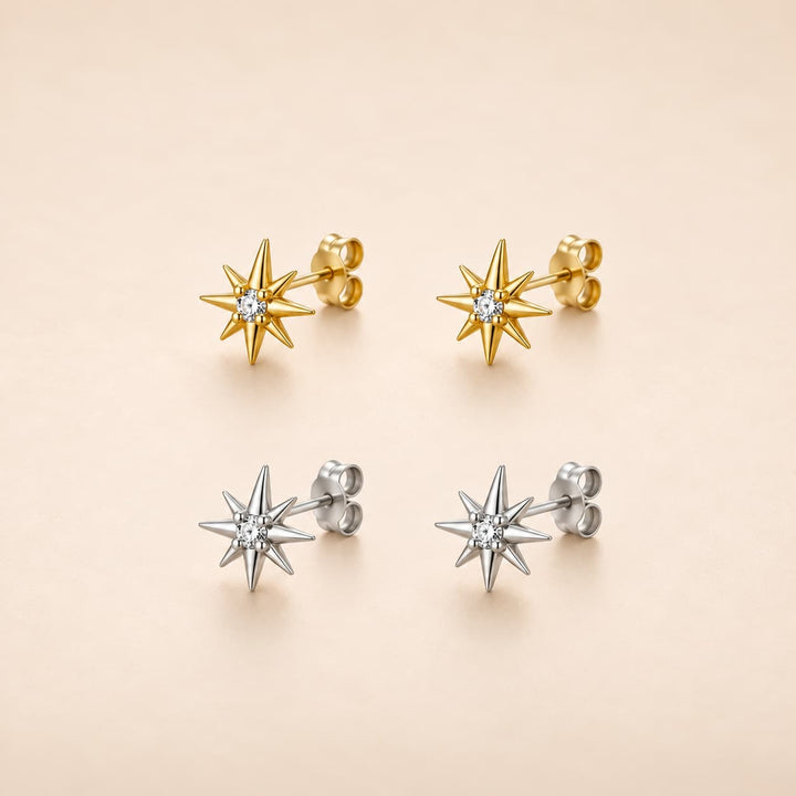 Four starburst stud earrings arranged in a 2x2 grid on a warm beige background. The top pair is gold-toned with a clear central stone, and the bottom pair is silver-toned with a clear central stone.